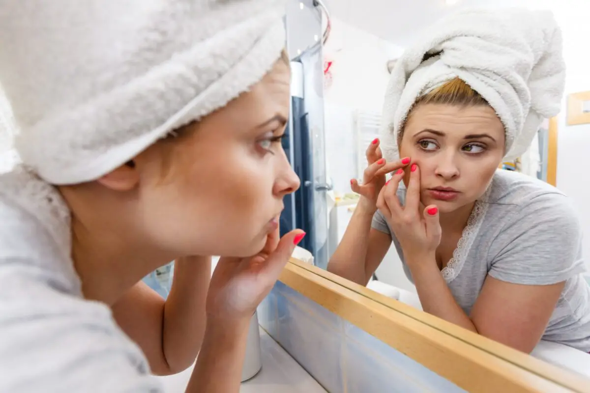 Woman looking in mirror dealing with acne